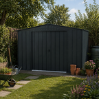 Duramax Dark gray metal garden shed in a backyard with plants and a wheelbarrow.